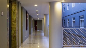 Een moderne hotelgang met een marmeren kolom, een glazen balustrade en uitzicht op de buitenkant van het gebouw.