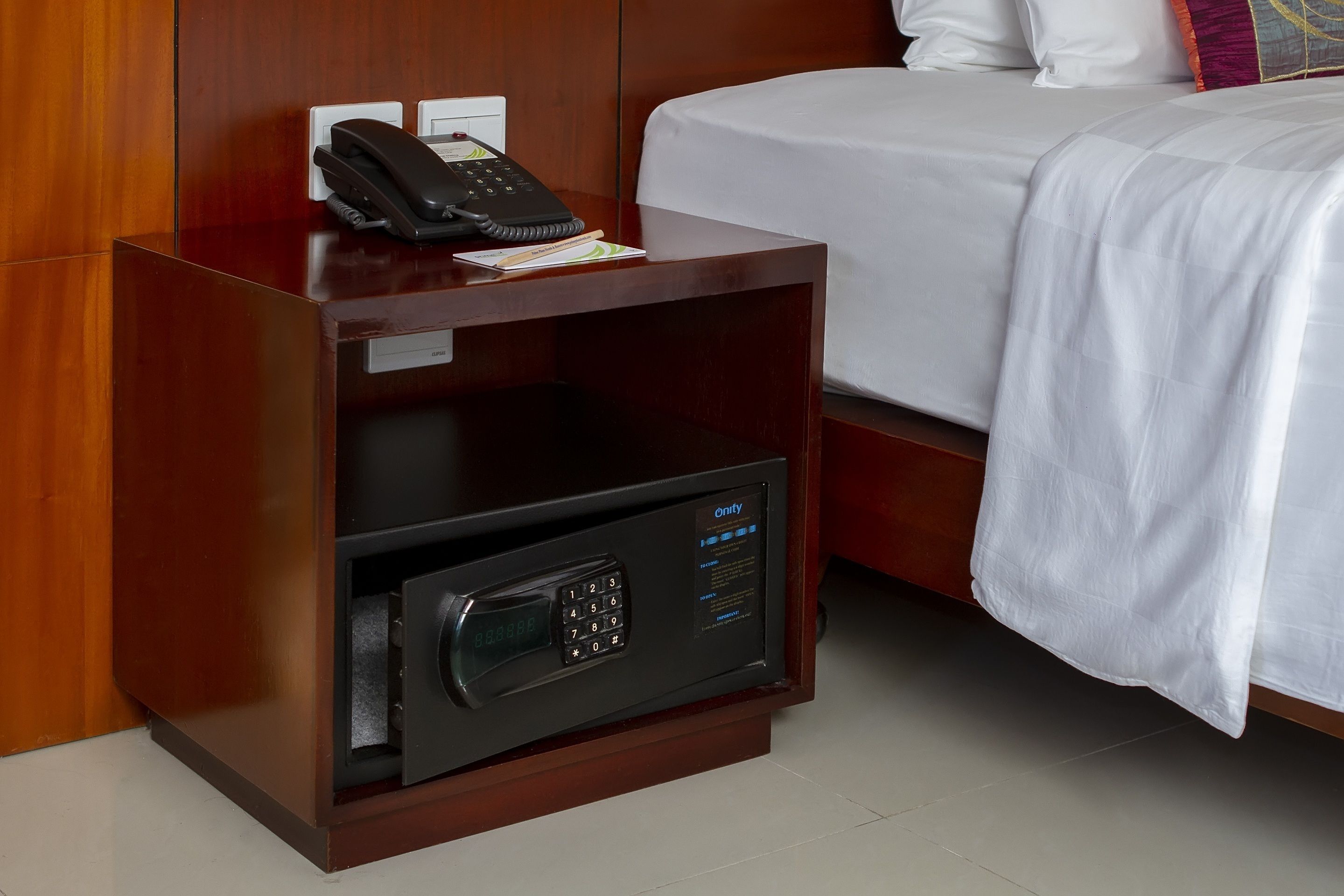 Habitación de hotel con mesita de noche de madera, teléfono y caja fuerte digital.