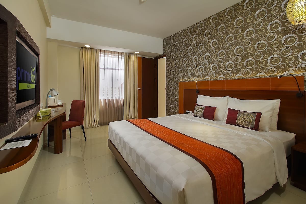 A hotel room with a bed, a desk, a TV, and a window with curtains.