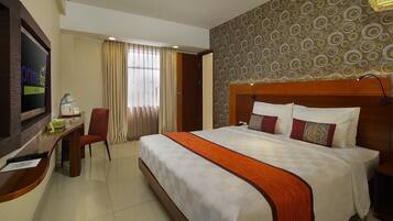 A hotel room with a bed, a desk, a TV, and a window with curtains.
