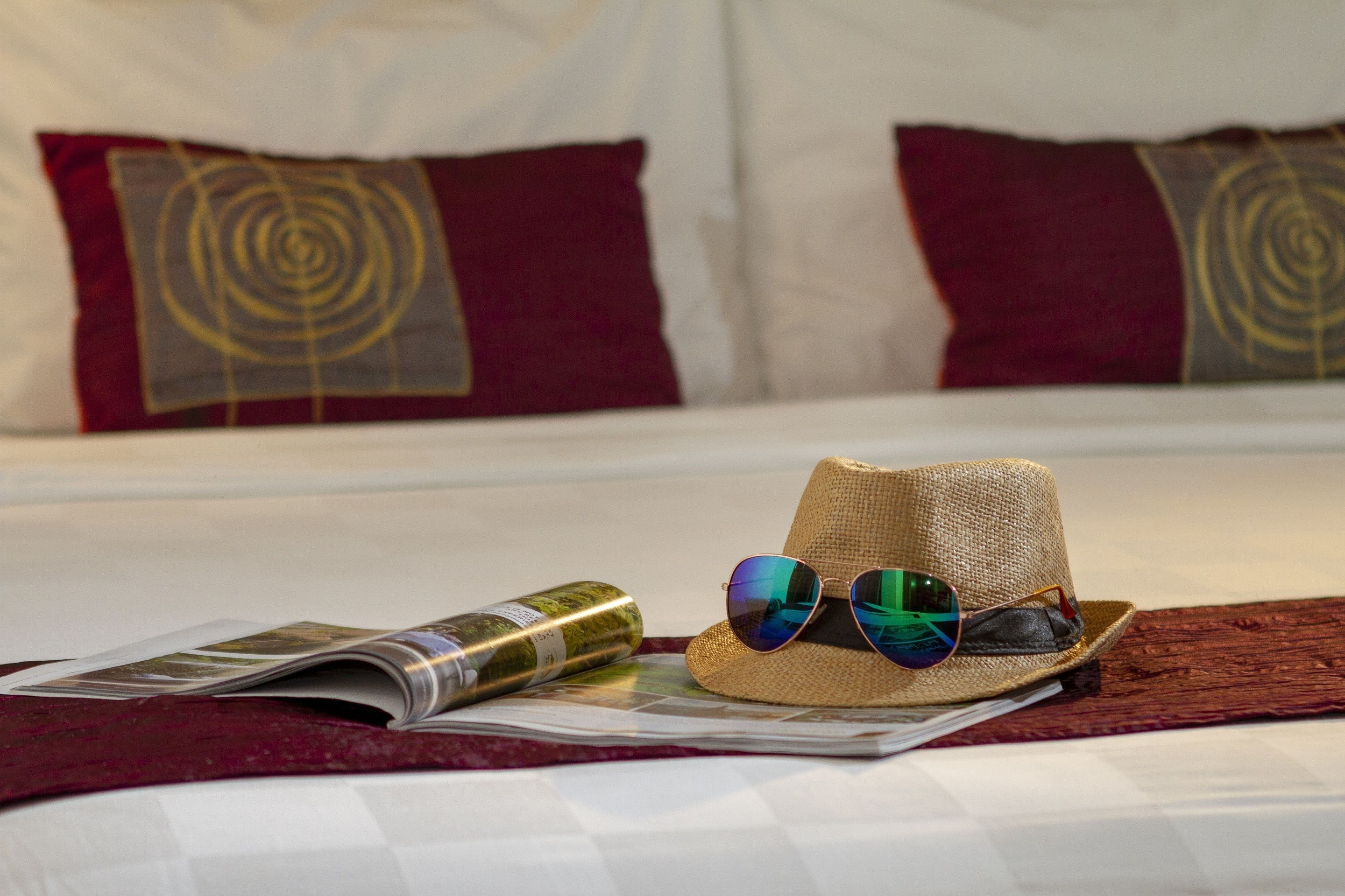 Una cama con una revista, un sombrero de paja y una botella de vino.