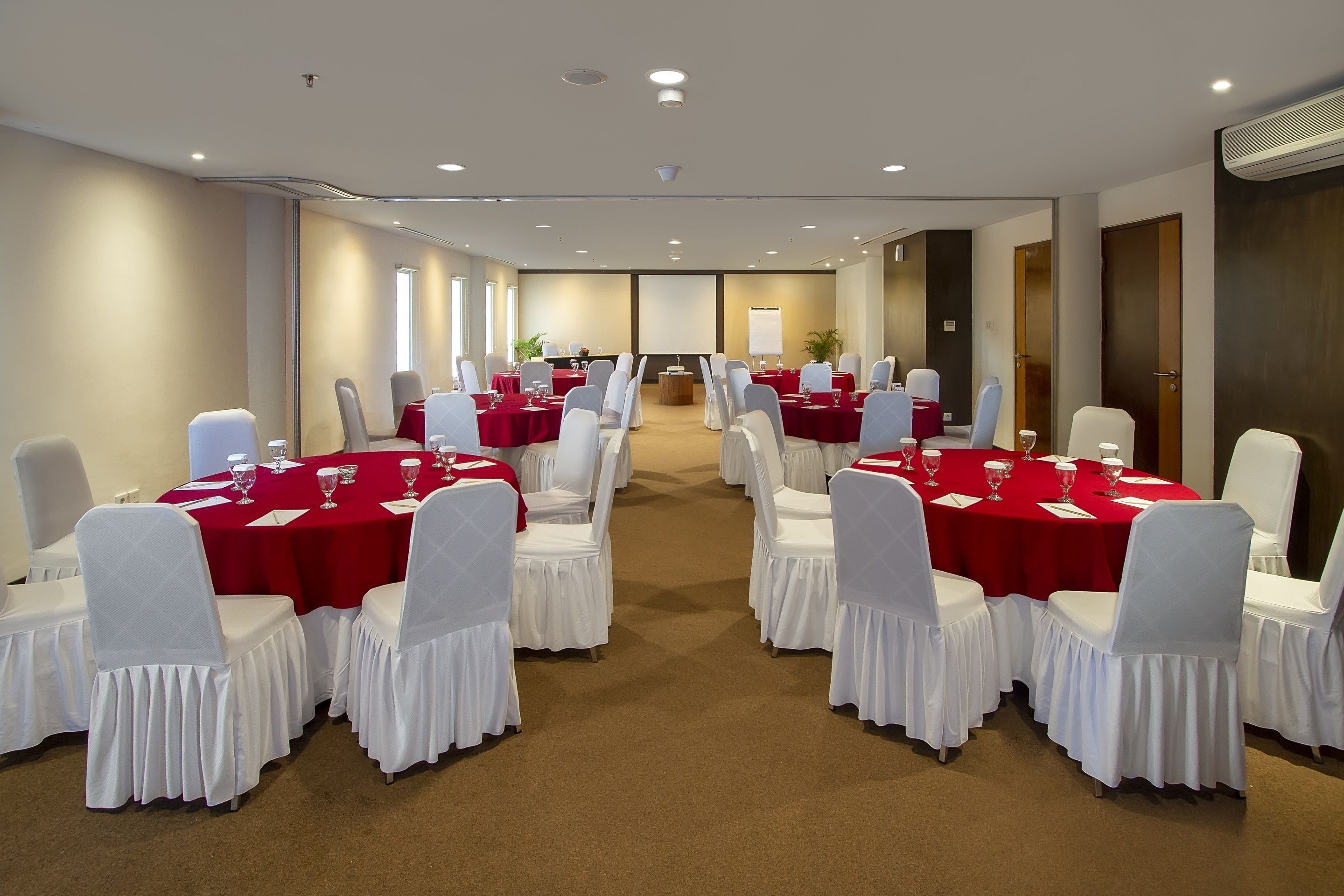 A conference room with multiple tables and chairs, arranged in rows, with red tablecloths and white chair covers.