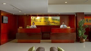 Een hotel receptie met twee baliemedewerkers, een groot landschapsschilderij en een receptiebalie.