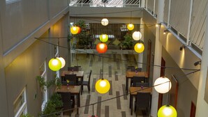 Een eethoek binnen met tafels, stoelen, hangende lichtjes en potplanten.