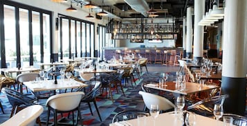 A modern restaurant interior with multiple dining tables, chairs, and a bar area.