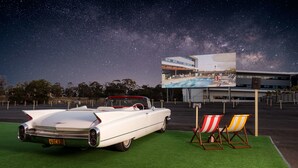 A white convertible car parked on artificial grass with beach chairs nearby, under a night sky with stars. - Atura Blacktown (Prospect)