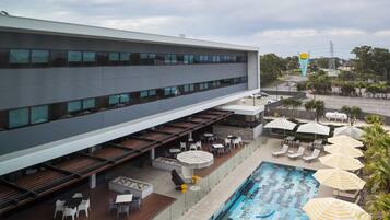 A modern building with a rooftop pool area, outdoor seating, and umbrellas.