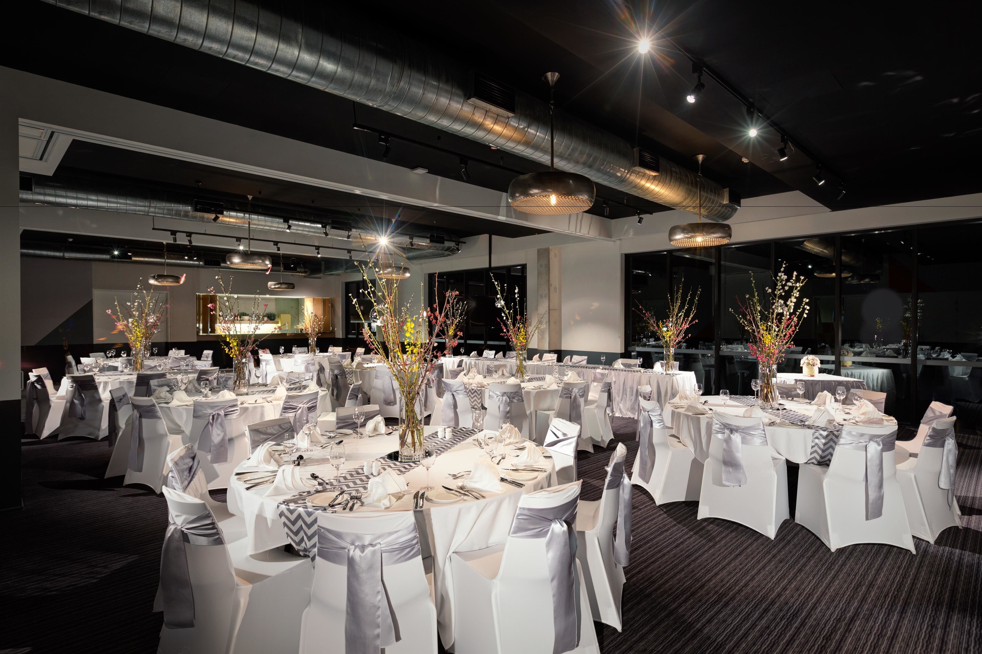 Un salón de banquetes con mesas redondas, manteles blancos y sillas con cintas grises.