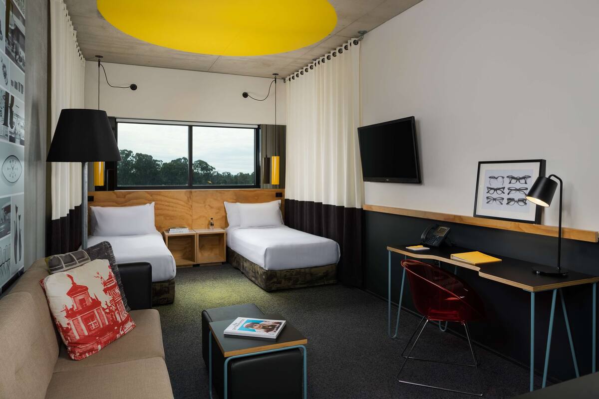A hotel room with two beds, a desk, a chair, a TV, and a window with a view.
