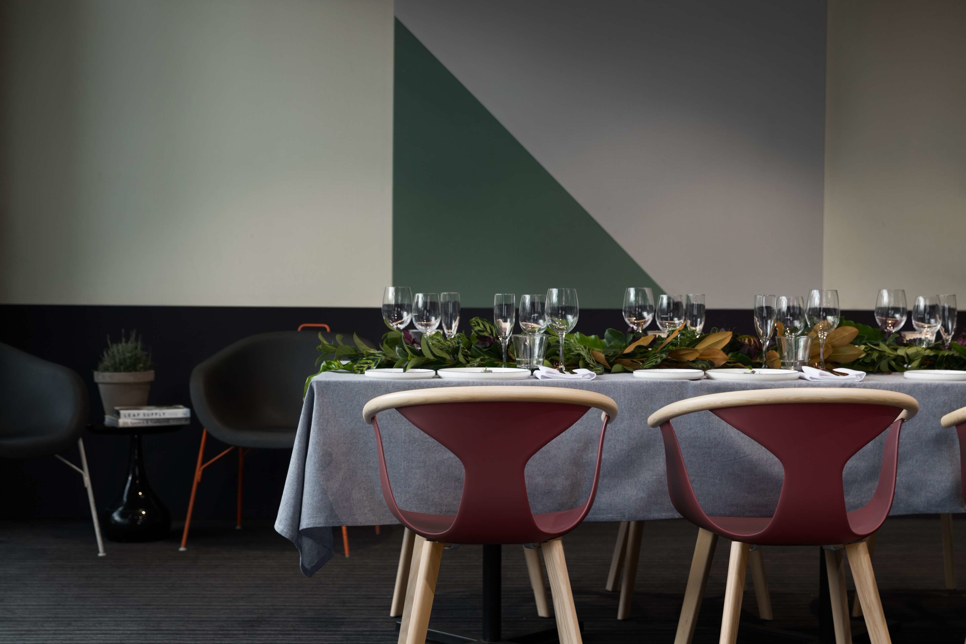 A dining area with a long table set for a meal, surrounded by modern chairs with wooden legs.
