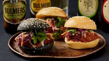 Deux hamburgers sur une assiette en bois, avec une bouteille de cidre à la poire Bulmers en arrière-plan.