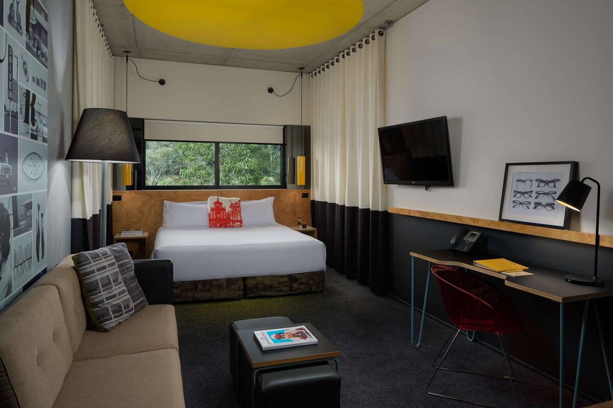 A hotel room with a bed, a desk, a chair, a couch, and a TV.