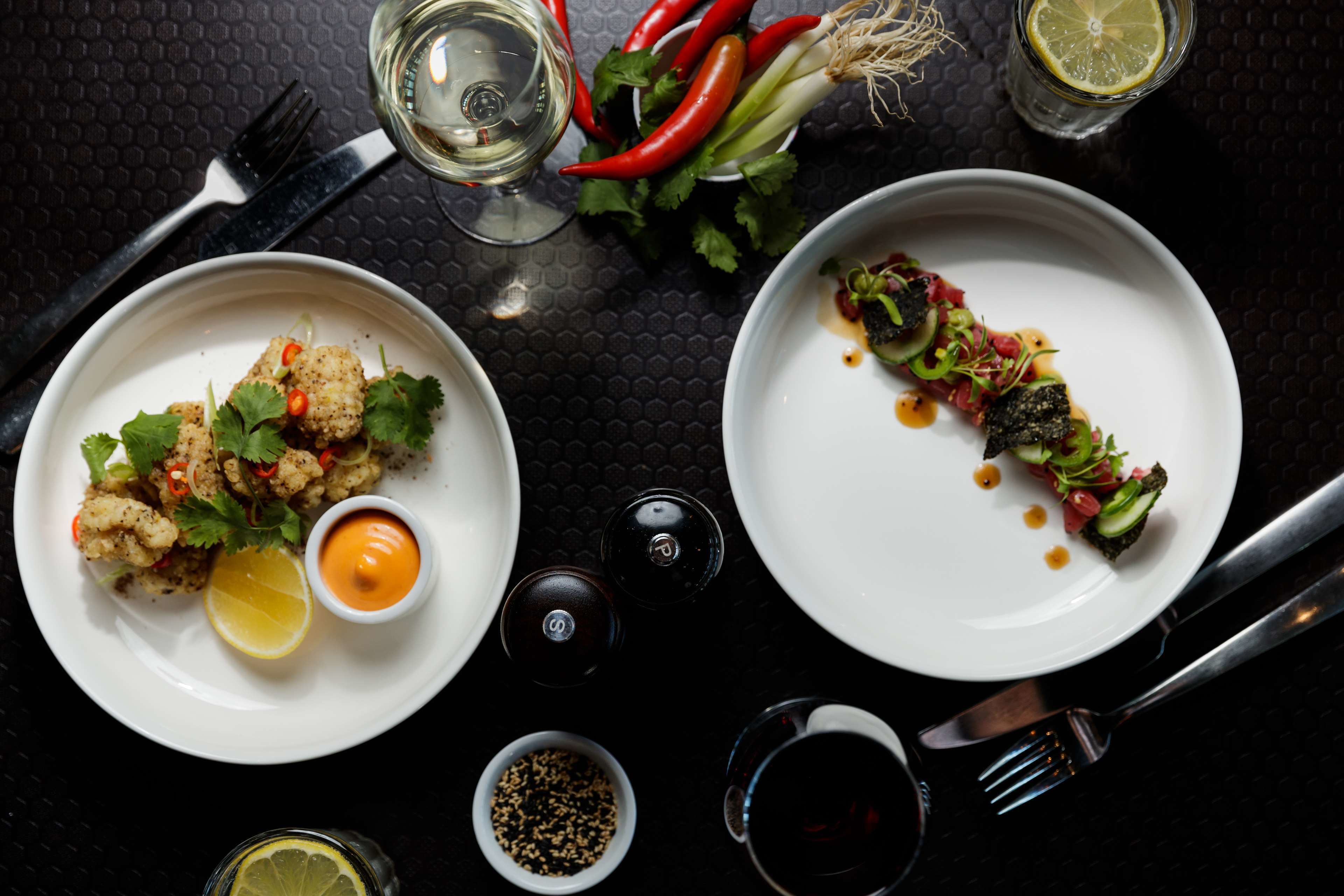 Deux assiettes de nourriture, accompagnées de condiments, et un verre de vin rouge, sur une table.