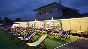 A row of beach chairs on artificial grass in front of a building with a sloped roof and a light pole. - Atura Blacktown (Prospect)