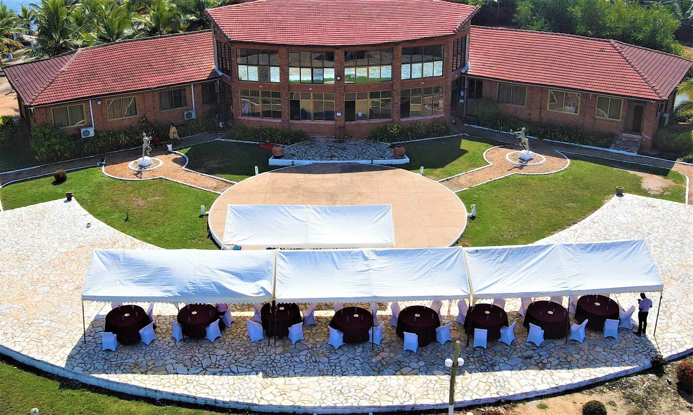 A building with a red-tiled roof and large windows, surrounded by a landscaped garden with a central circular area and outdoor seating.