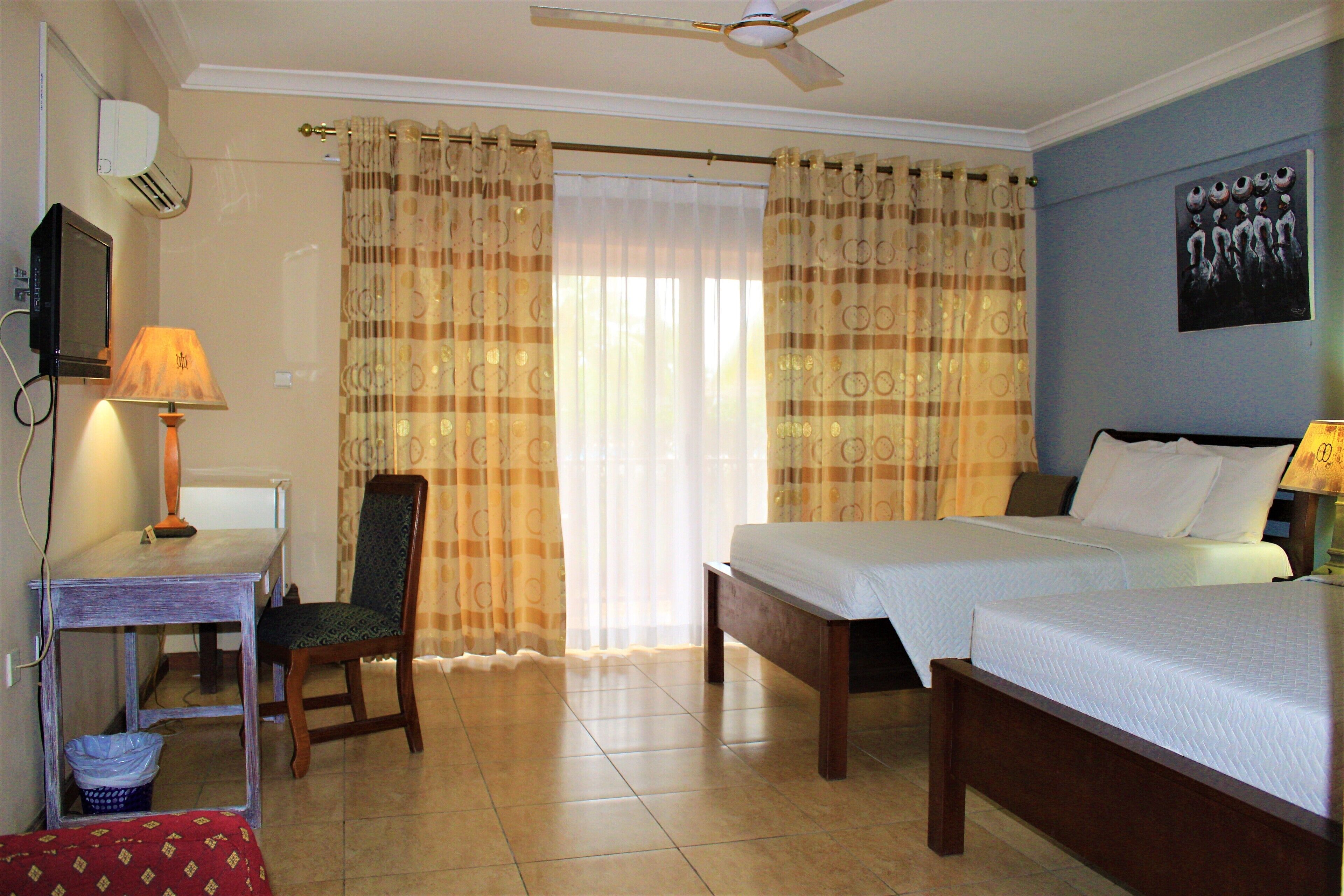 Habitación de hotel con dos camas, un escritorio, una silla, un televisor y un ventilador de techo.