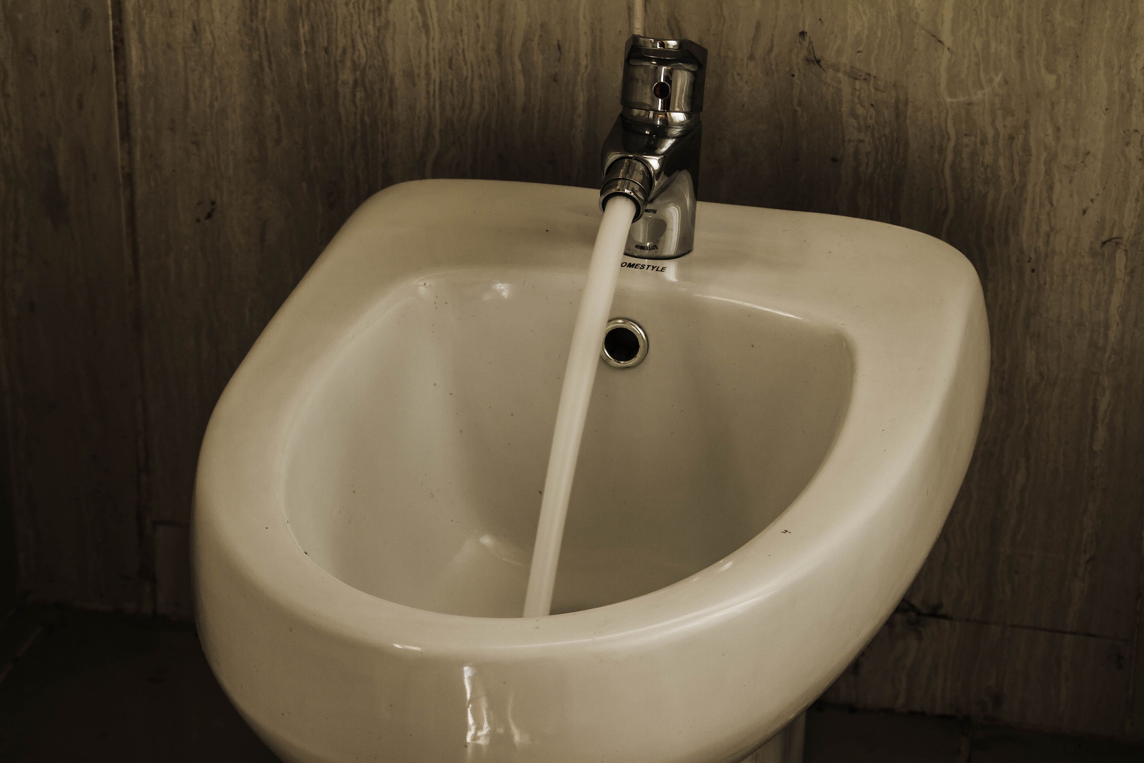 A white urinal with a chrome faucet and a drain.