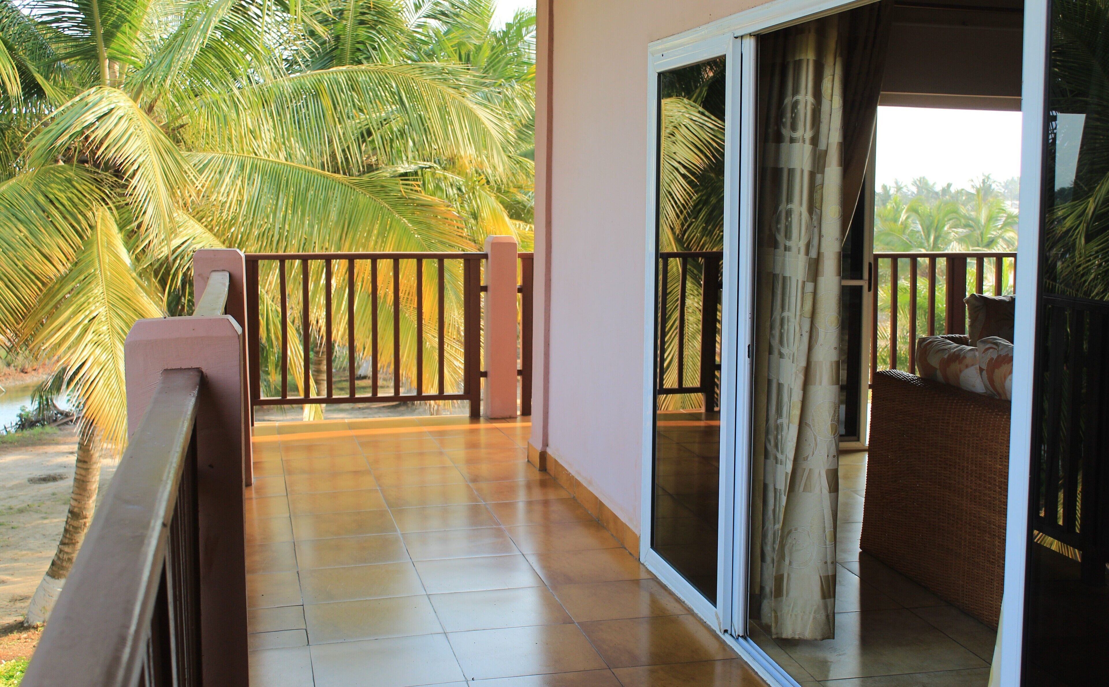A balcony with a tiled floor, a wooden railing, and a view of palm trees.