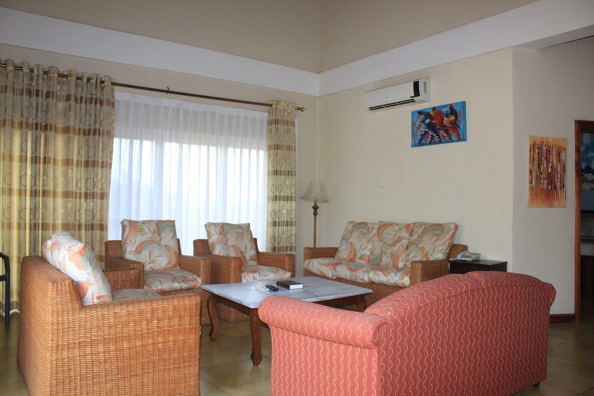 A living room with wicker furniture, a red sofa, and a table with a book and remote control.
