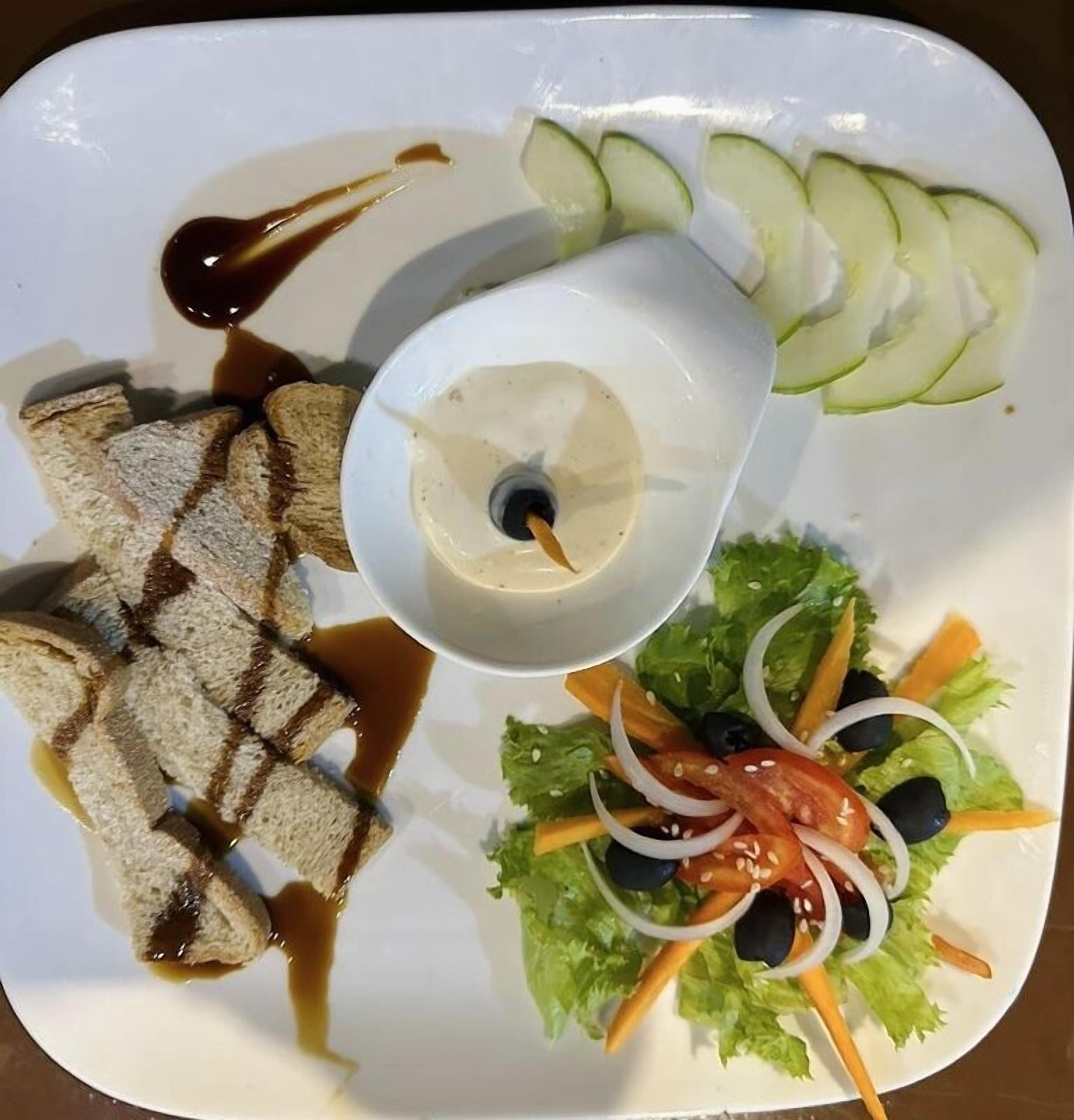 Un plato con pan a la parrilla, ensalada y un recipiente pequeño con salsa.