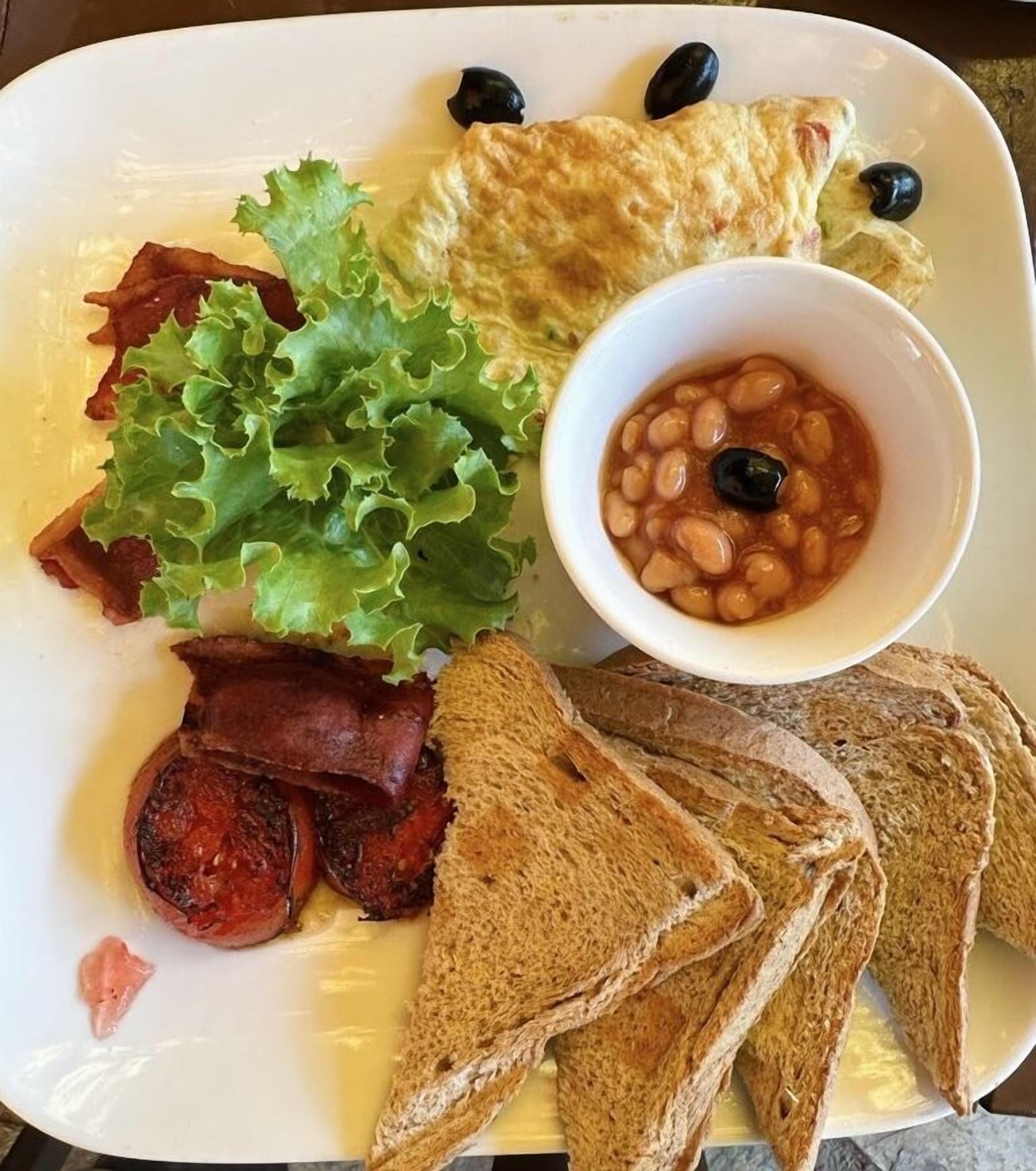 A breakfast plate with bacon, toast, eggs, beans, and lettuce.