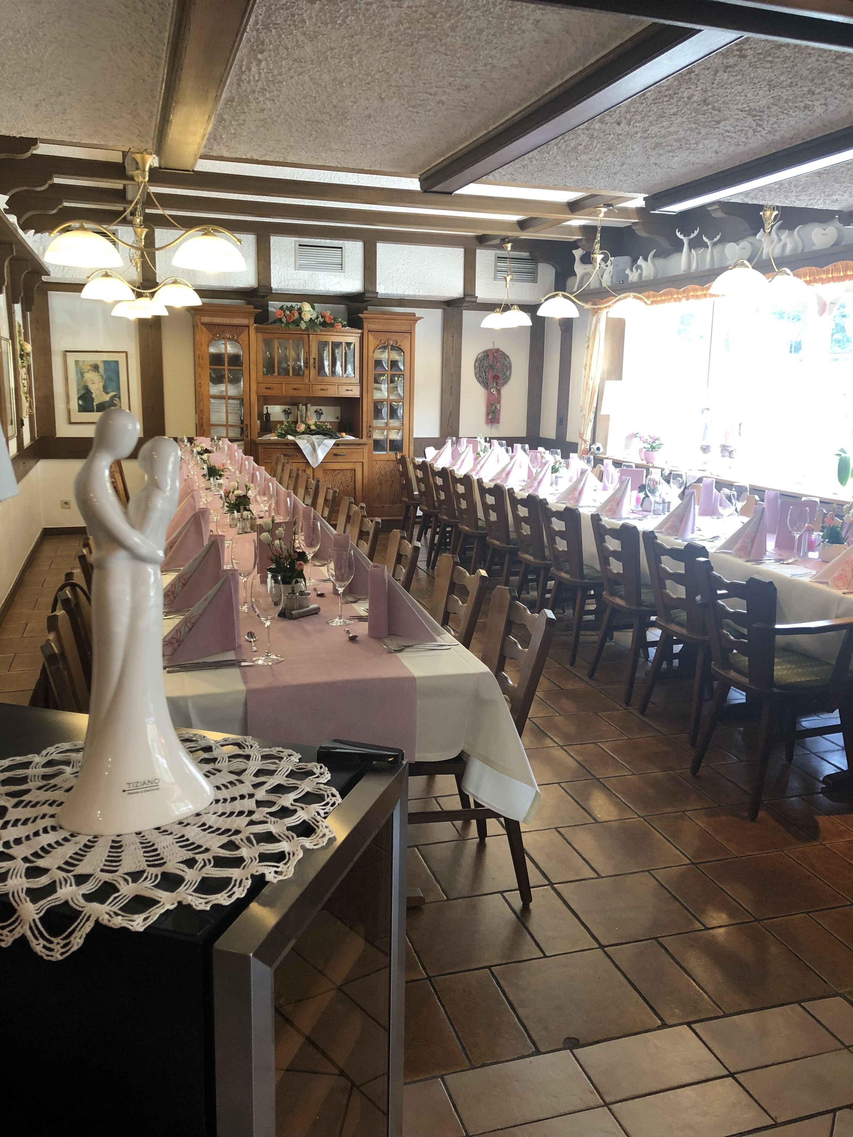 A restaurant with a long dining table set for a meal, wooden chairs, and a decorative white vase on the table.