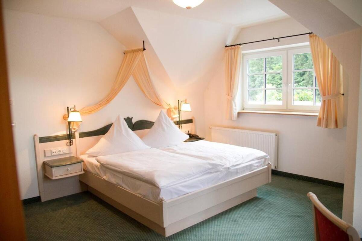 A single-bed room with a canopy bed, bedside lamps, a nightstand, and a window with curtains.