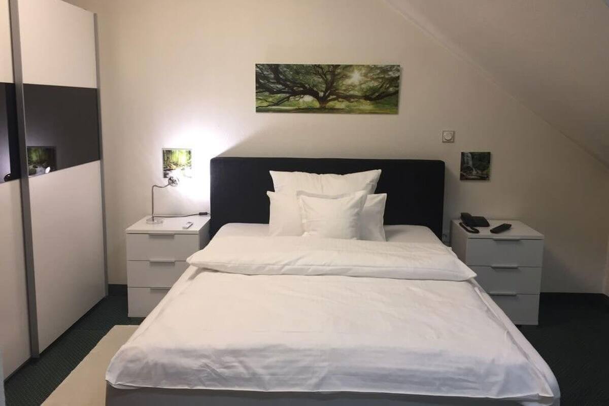 A bedroom with a bed, two bedside tables, a nightstand, a wardrobe, and a painting on the wall.