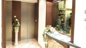 A room with a wooden ceiling, a large window with a view of a kitchen, and a small table with a vase of flowers. - Landhotel Menke (Brilon)