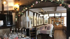 A restaurant with a long dining table, a bar area with bottles and glasses, and a wooden ceiling with decorative flowers. - Landhotel Menke (Brilon)