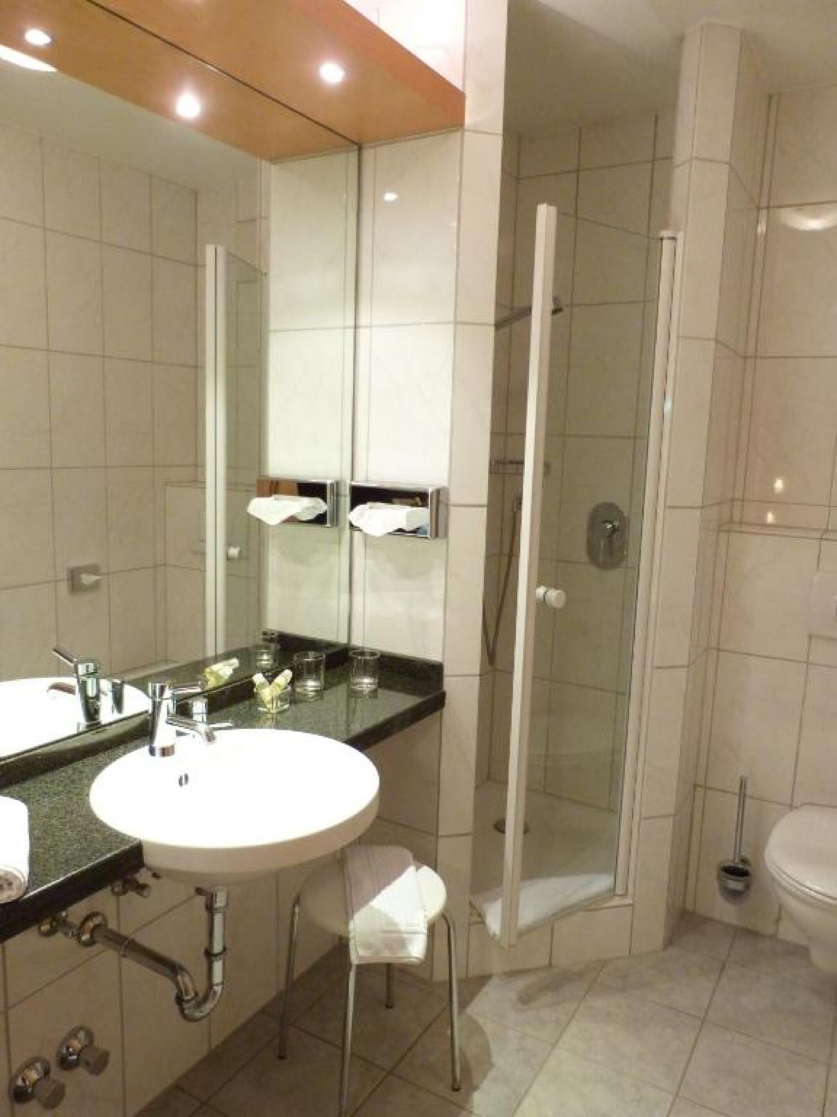 A modern bathroom with a large mirror, two sinks, a shower enclosure, and a toilet.