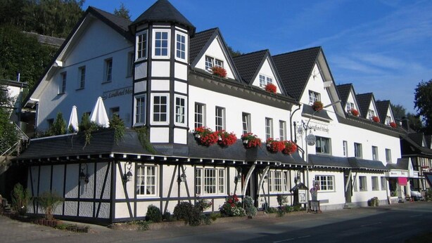 A traditional half-timbered building with a prominent tower, multiple windows, and flower boxes on the upper floors. - Landhotel Menke (Brilon)