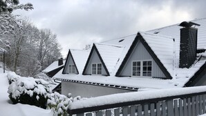 A house with a steeply pitched roof covered in snow, a wooden fence, and snow-covered trees. - Landhotel Menke (Brilon)