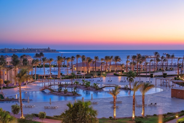A resort with a large pool, palm trees, and a view of the ocean at sunset. - Cleopatra Luxury Resort Makadi Bay (Makadi Bay)