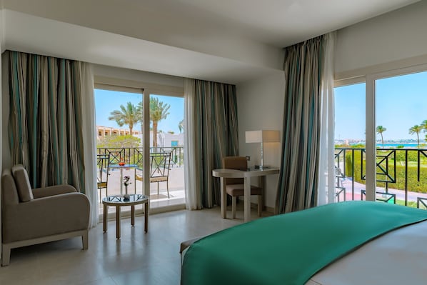 Une chambre d’hôtel comprenant un lit, un bureau, une chaise et un balcon avec vue sur les palmiers et les immeubles.