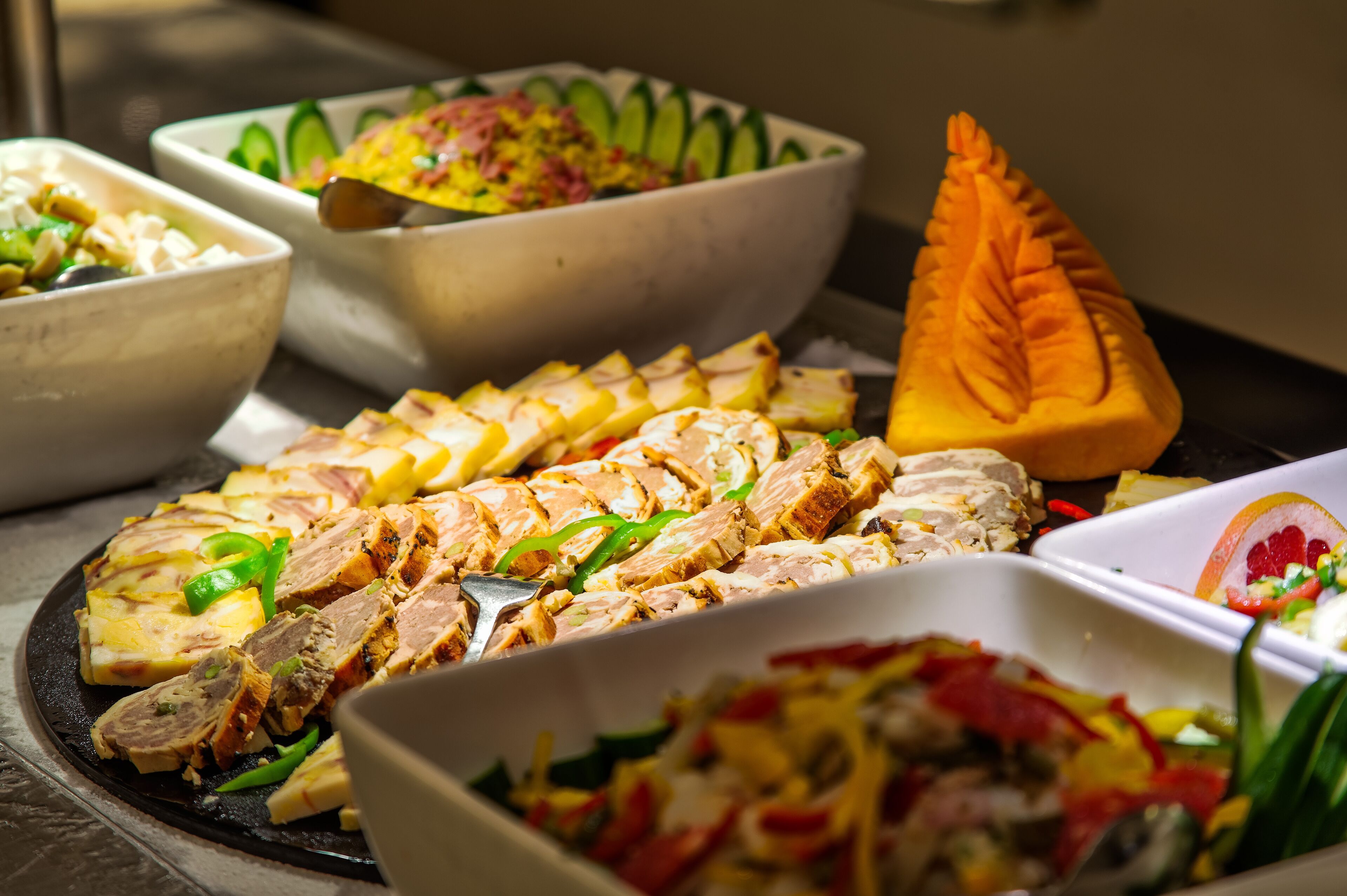 A buffet with various dishes including sliced meat, vegetables, and a carved orange.