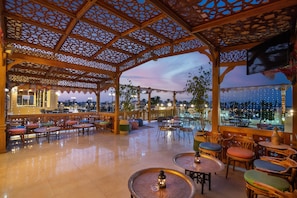 An outdoor seating area with wooden tables and chairs, a view of the cityscape, and a decorative ceiling. - Cleopatra Luxury Resort Makadi Bay (Makadi Bay)