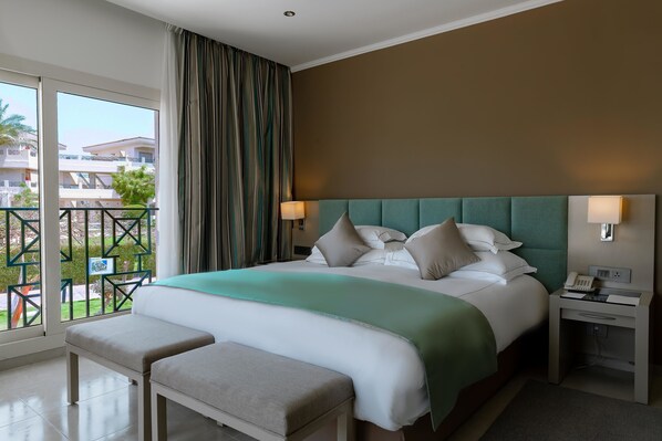 A hotel room with a large bed, a bench, a nightstand, and a view of the outside balcony.