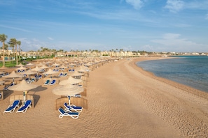 A beach with rows of sun loungers and umbrellas, palm trees, and a hotel in the background. - Cleopatra Luxury Resort Makadi Bay (Makadi Bay)