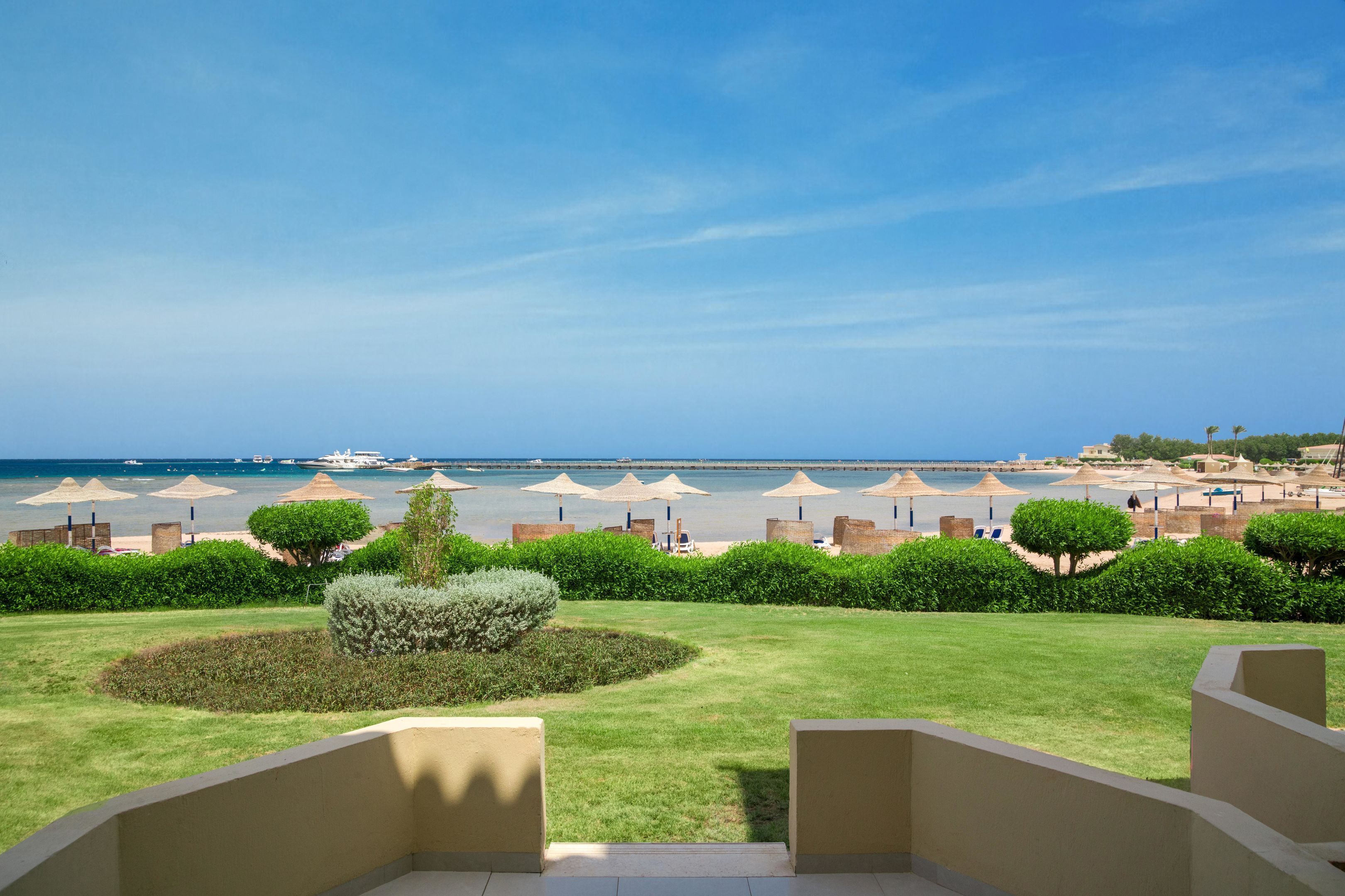 Vista de un resort con piscina, sombrillas y una playa al fondo.
