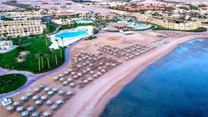 Vue aérienne d’un complexe hôtelier doté d’une grande piscine, de nombreux parasols installés sur la plage et de différents bâtiments d’hôtel.