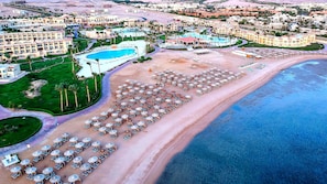 Luchtbeeld van een resort met een groot zwembad, diverse parasols aan het strand en verschillende hotelgebouwen.