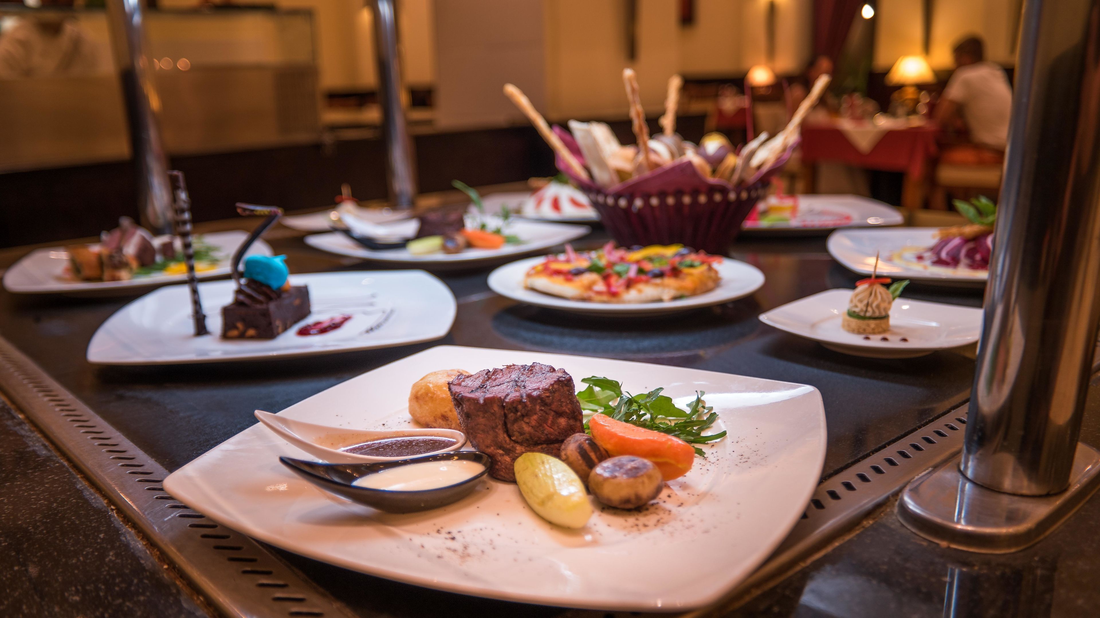 A buffet table with various plated dishes including a steak, vegetables, and desserts.