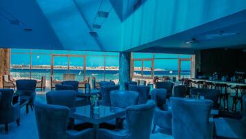 Ein großzügiger Innenbereich mit einem großen Fenster und Blick auf die Küste, der verschiedene Sitzgelegenheiten und eine Bar bietet.