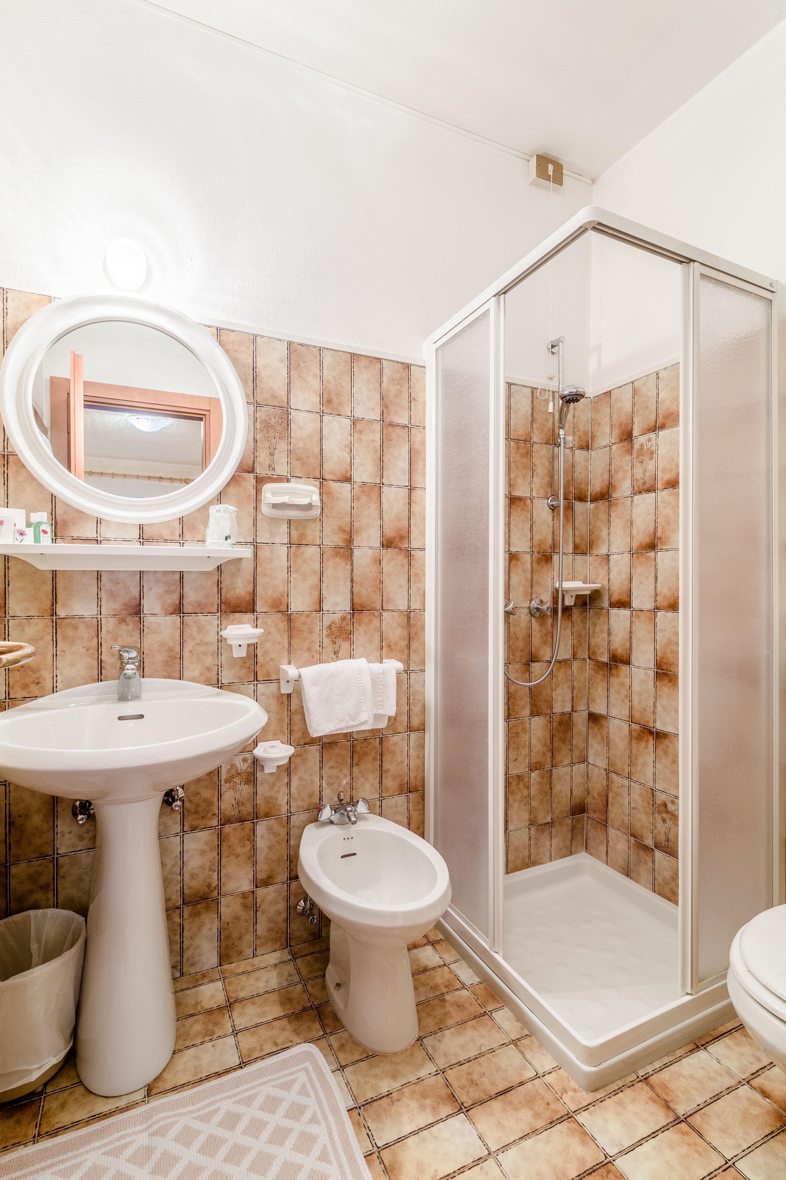 Baño con lavamanos, bidé, inodoro y ducha con mampara de vidrio.