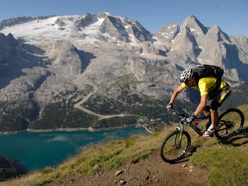 A mountain biker on a trail with a lake and mountains in the background.
