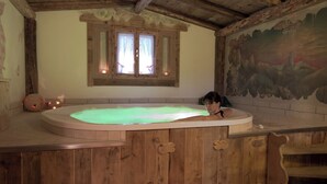 A wooden bathtub with a greenish water feature, a window with curtains, and a mural on the wall. - Pineta Pastry Hotel (Rocca Pietore)