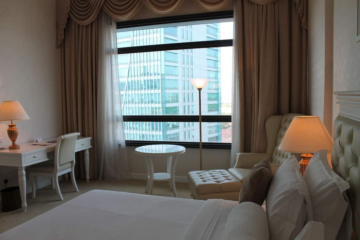 A hotel room with a bed, a desk, a chair, a round table, and a lamp.
