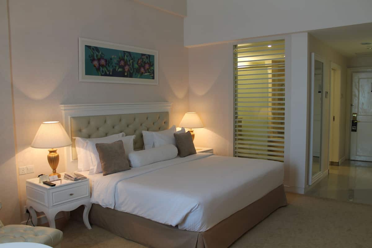A neatly arranged bedroom with a large bed, two bedside tables with lamps, a headboard, and a painting on the wall.