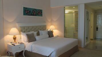 A neatly arranged bedroom with a large bed, two bedside tables with lamps, a headboard, and a painting on the wall.